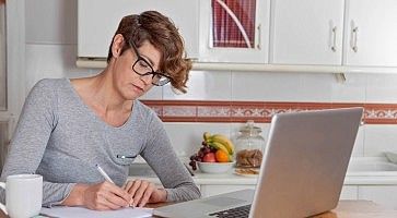 Una ragazza concentrata davanti al computer, scrivere su un foglio alcuni appunti.