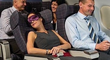 Una donna dorme in aereo, con una mascherina sul viso.