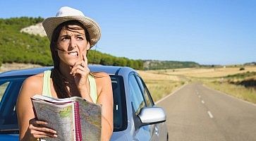 Una ragazza davanti ad un'auto, guarda la mappa con la faccia titubante.