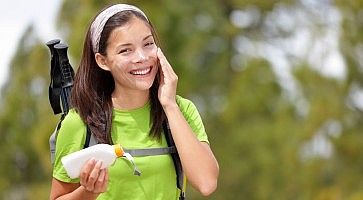 Ragazza che fa trekking e si applica la crema da sole al viso.