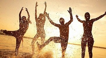 Silhouette di un gruppo di persone mentre si divertono saltando nell'acqua del mare al tramonto.