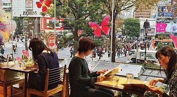 Persone sedute ai tavoli vicino alle finestre all'Occitane Cafe a Shibuya, sullo sfondo il famoso incrocio.