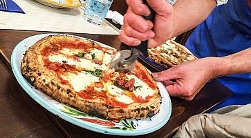 Un cameriere taglia una pizza margherita con un pizza cutter.