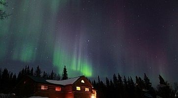 Aurora boreale in Alaska, sopra una casa in mezzo ai boschi.