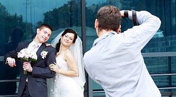 Un fotografo al lavoro mentre fotografa due sposi in posa.
