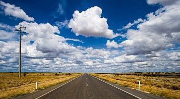 Strada deserta e diritta, con un cielo ricco di splendide nuvole.