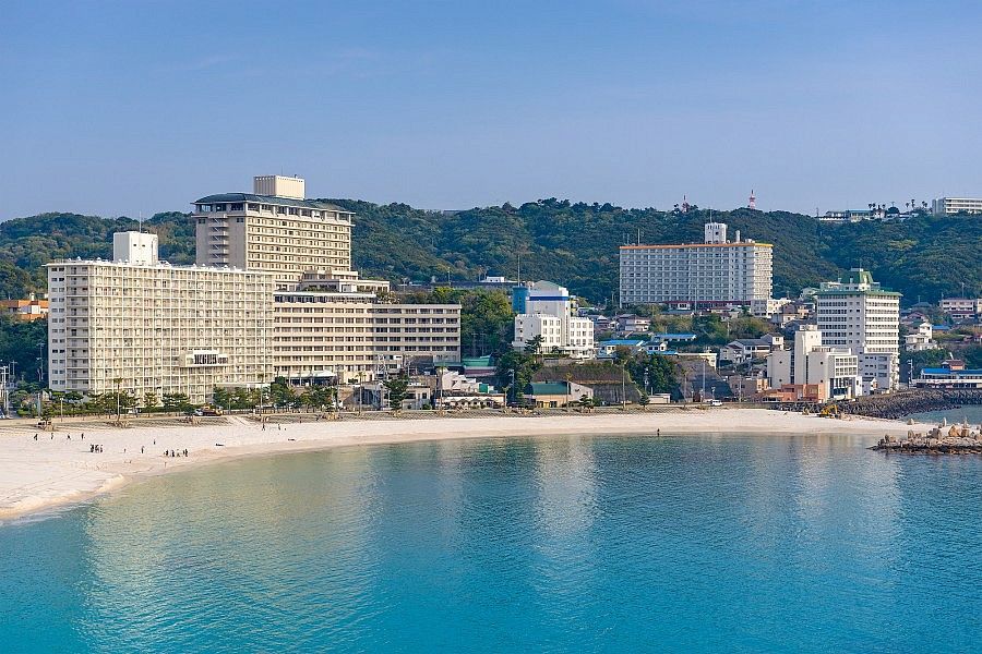 Spiaggia di Shirahama con edifici sulla riva e colline verdi sullo sfondo.