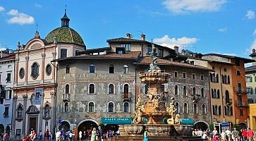 Piazza Duomo a Trento, la fontana in primo piano e dietro dei raffinati affreschi.