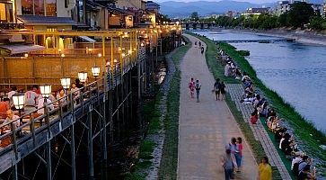 Persone camminano al tramonto sulle rive del fiume Kamogawa a Kyoto.