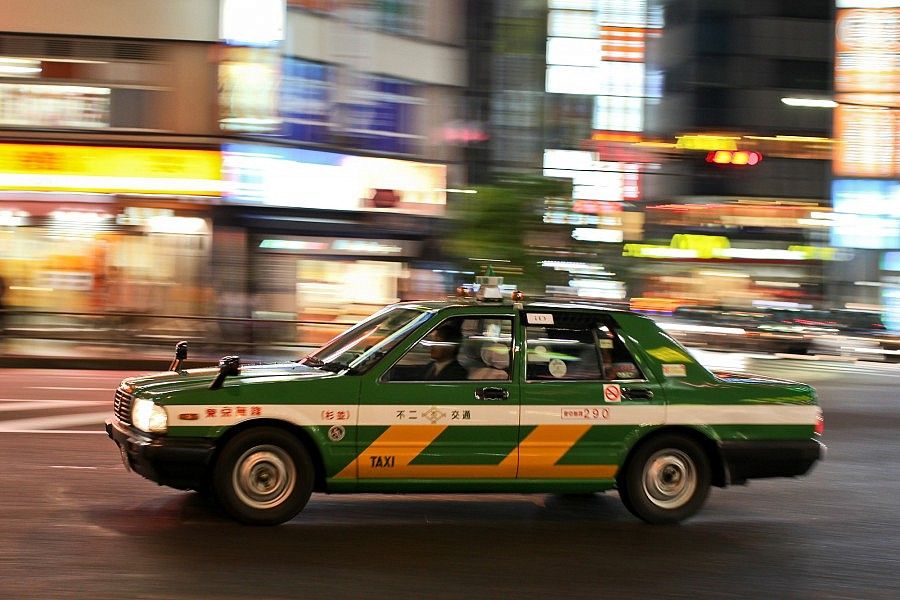 Taxi verde e giallo in movimento per le strade illuminate di Tokyo.