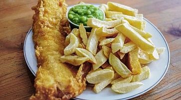 English battered Cod Fish and Chips with Mushy Peas in a plate on a table top