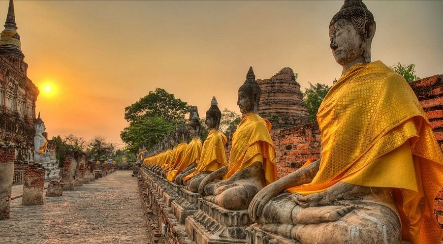 Statue di Buddha in fila con abiti gialli al tramonto in Thailandia.