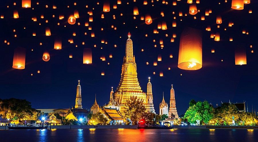Lanterns volano sopra il tempio Wat Arun illuminato di notte in Thailandia.