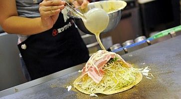Una cameriera intenta nella preparazione di un okonomiyaki.