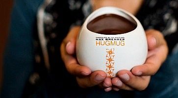 Una persona tiene tra le mani una tazza "Hugmug" piena di cioccolato, da Max Brenner.