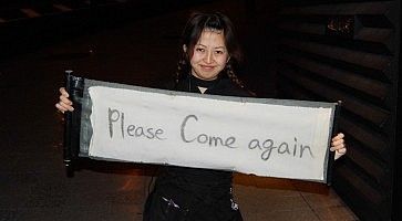 Cameriera tiene in mano uno striscione per invitare i clienti a tornare ancora, al ristorante Ninja di Akasaka.