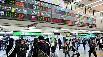 Tabelloni con orari dei treni e persone nell'immensa stazione di Shinjuku.